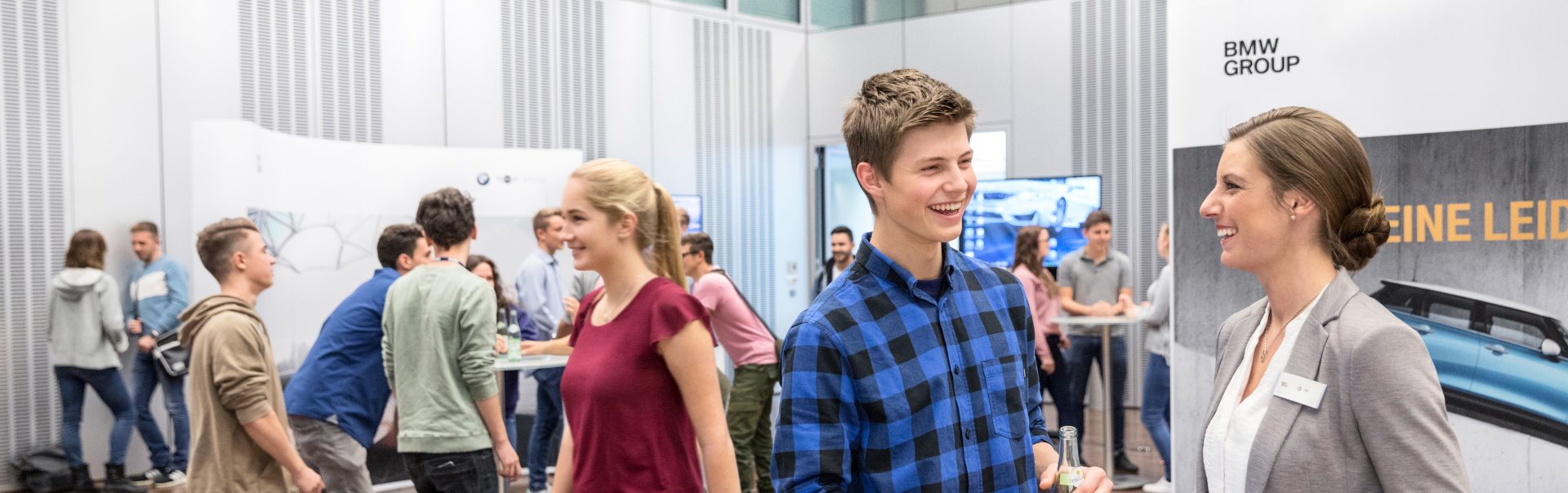 Zwei Azubis unterhalten sich in der Werkstatt der BMW Group vor einem BMW iX.