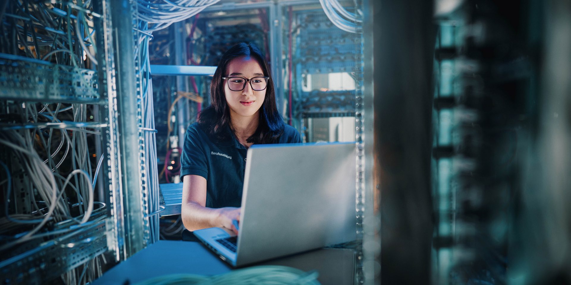 Eine Auszubildende, die an einem Laptop in einem Serverraum arbeitet.