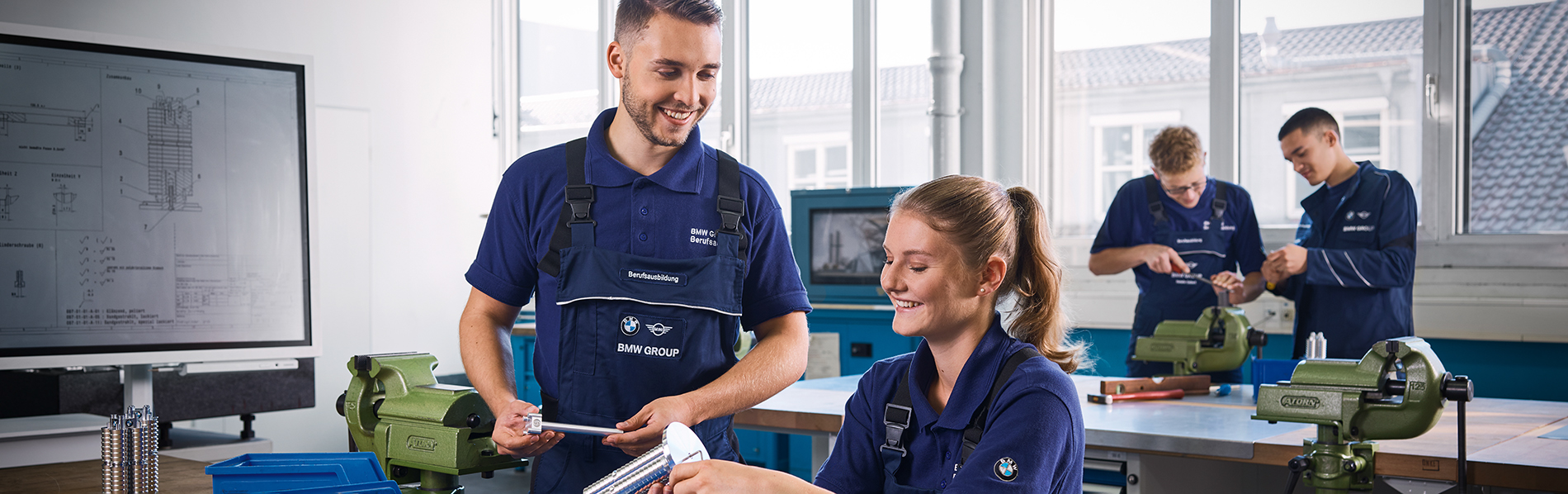 Vier Auszubildende, die in zweier Gruppen in einer Werkstatt bei der BMW Group arbeiten.