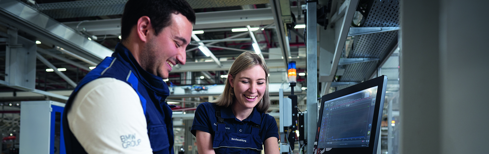 Eine Auszubildende mit ihrem Ausbilder in der Produktionshalle an einer Anlage