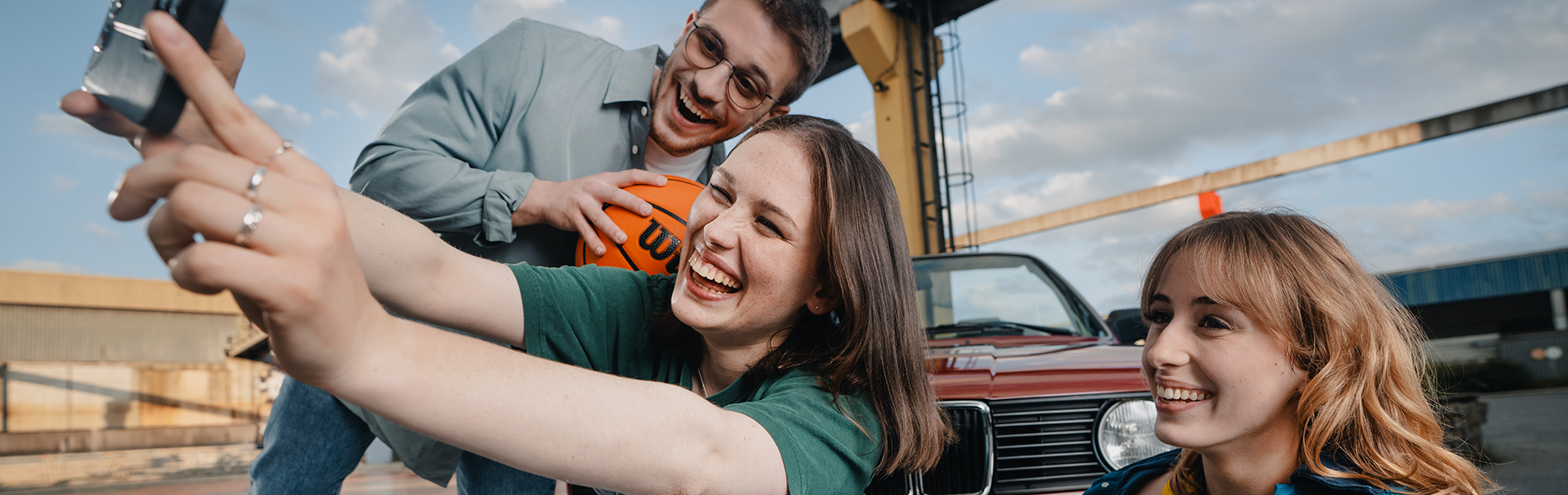 Drei Azubis machen ein Selfie vor einem Oldtimer-BMW.