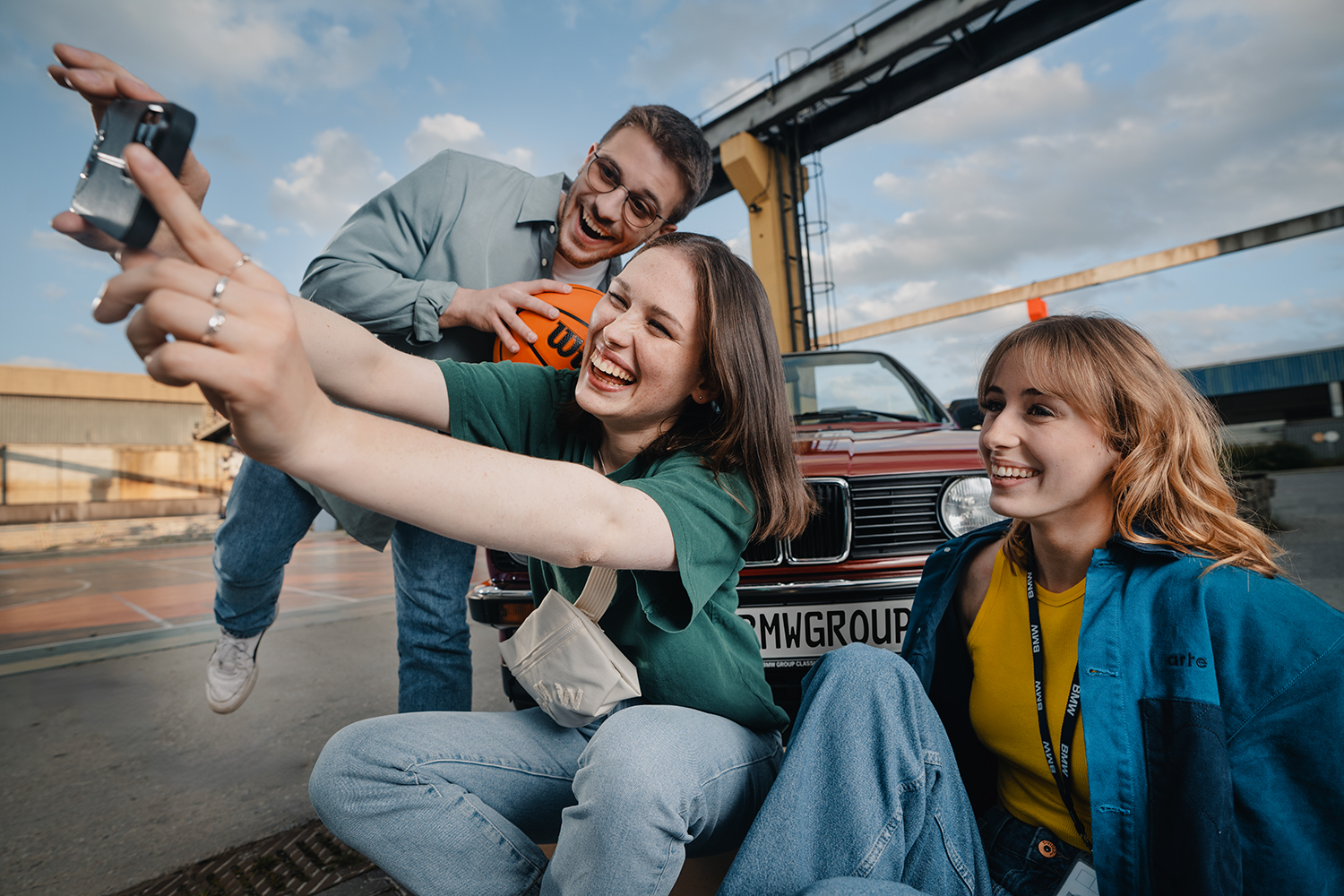 Drei Azubis machen ein Selfie vor einem Oldtimer-BMW.