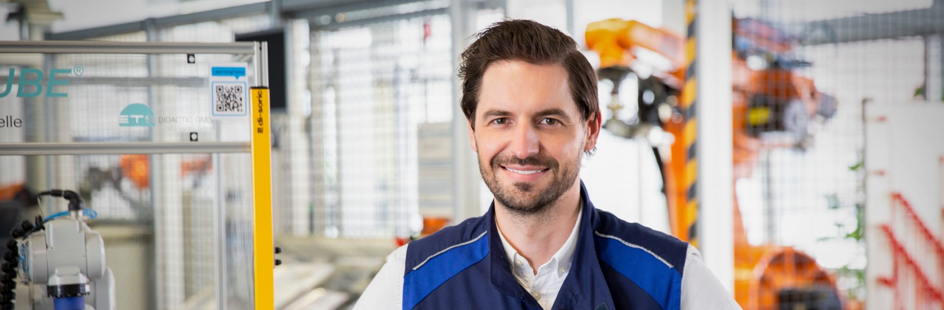 Lächelnder Ausbildungsleiter für technische Berufe und Studiengänge in einer modernen Fabrikumgebung.