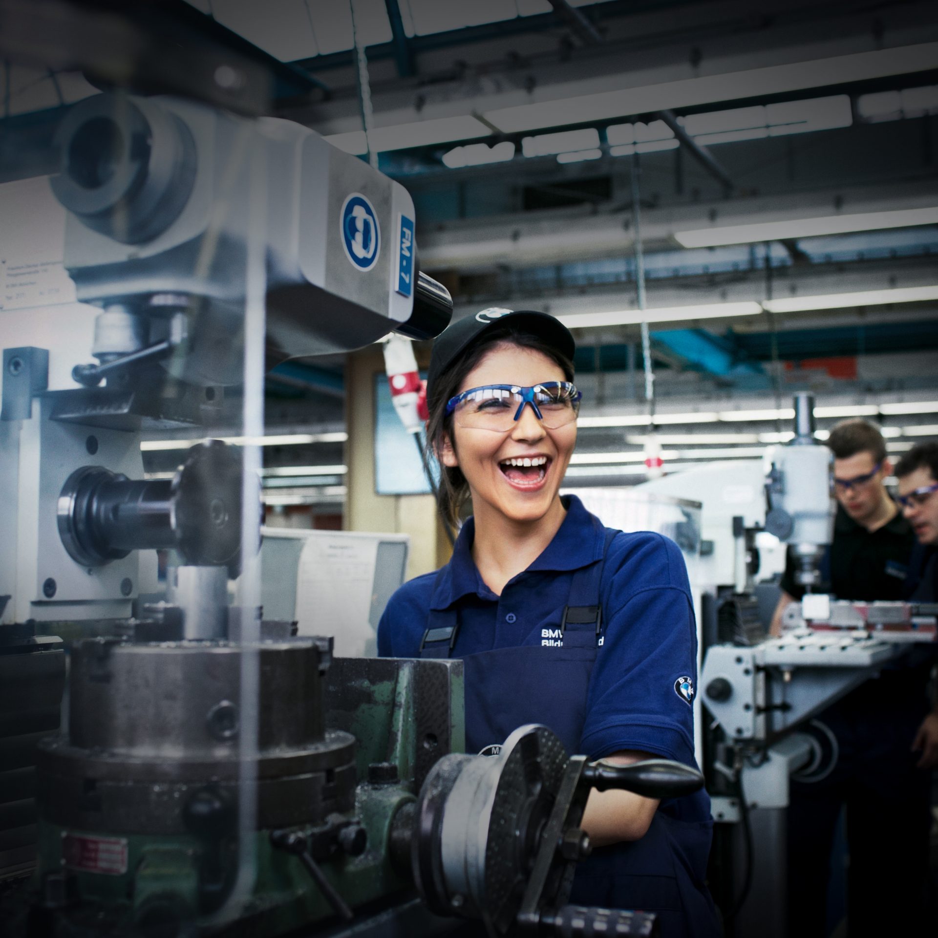 Auszubildende der BMW Group arbeitet lachend an der Drehmaschine.