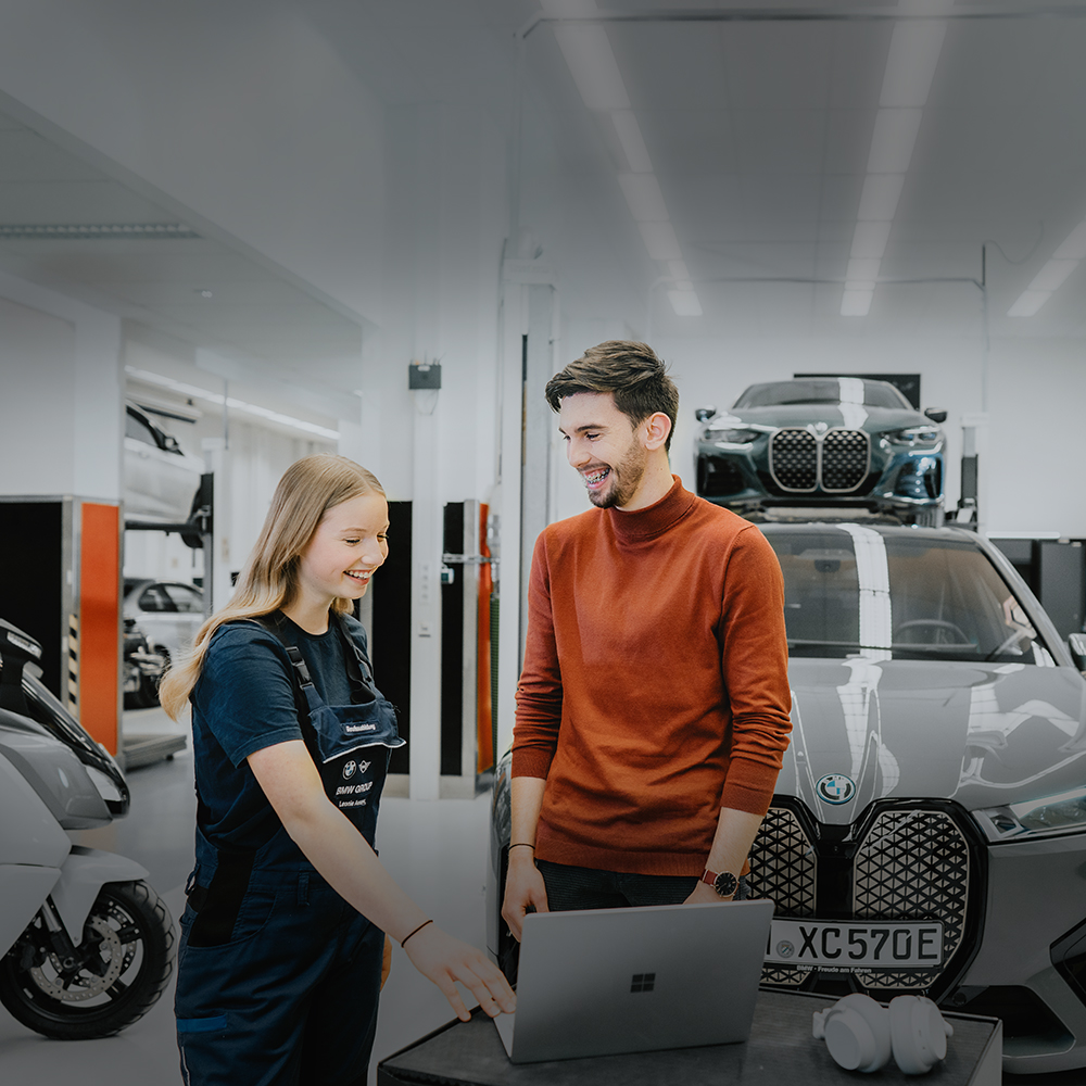 Zwei Azubis unterhalten sich in der Werkstatt der BMW Group vor einem BMW iX.