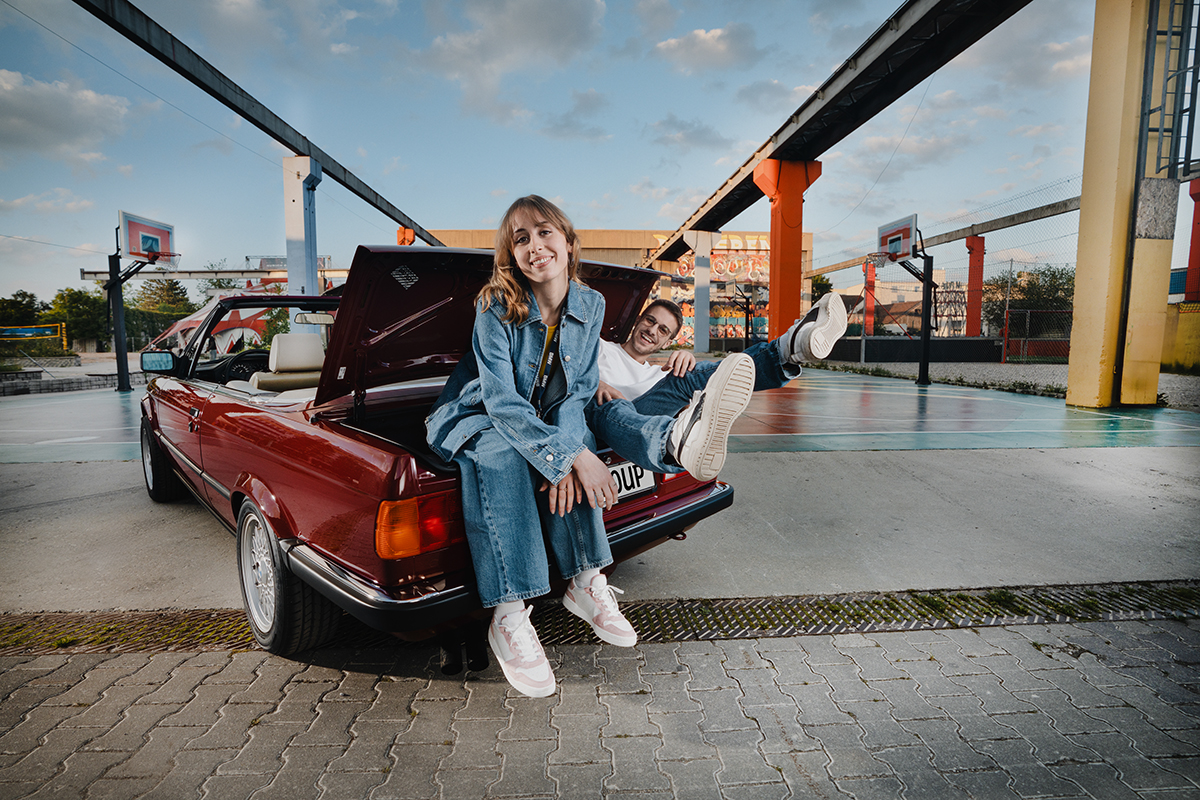 Zwei Azubis lachen und sitzen im Kofferraum eines BMW E30 Cabrios
