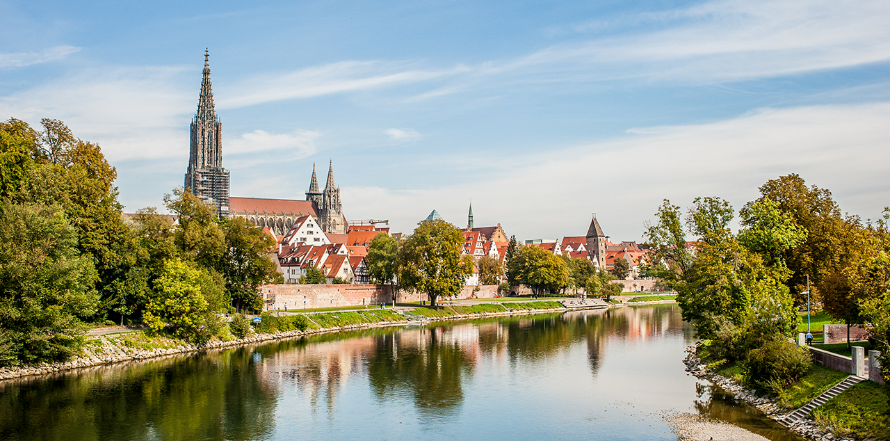Blick über den Fluss auf das Ulmer Münster vor einem blauen Himmel.