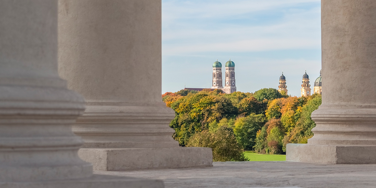 Die Münchener Frauenkirche durch die Säulen des Monopteros im Englischen Garten fotografiert.