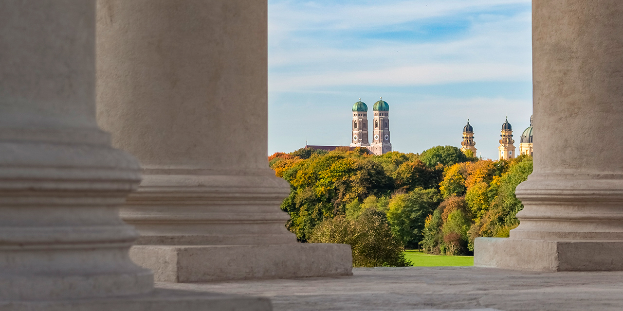 Die Münchener Frauenkirche durch die Säulen des Monopteros im Englischen Garten fotografiert.