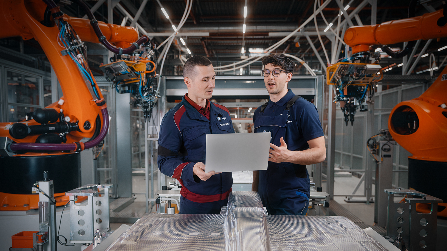Zwei Instandhalter bei der Arbeit am am LapTop zwischen Roboterarmen.