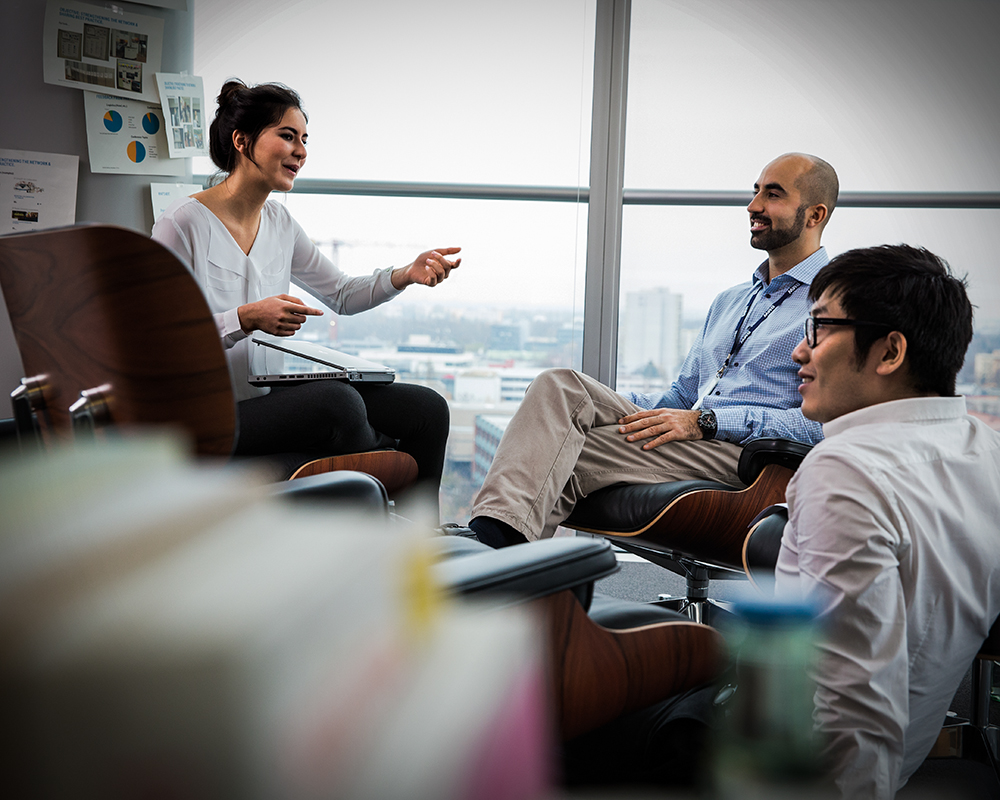 Drei Mitarbeiter der BMW Group sitzen zusammen und unterhalten sich.