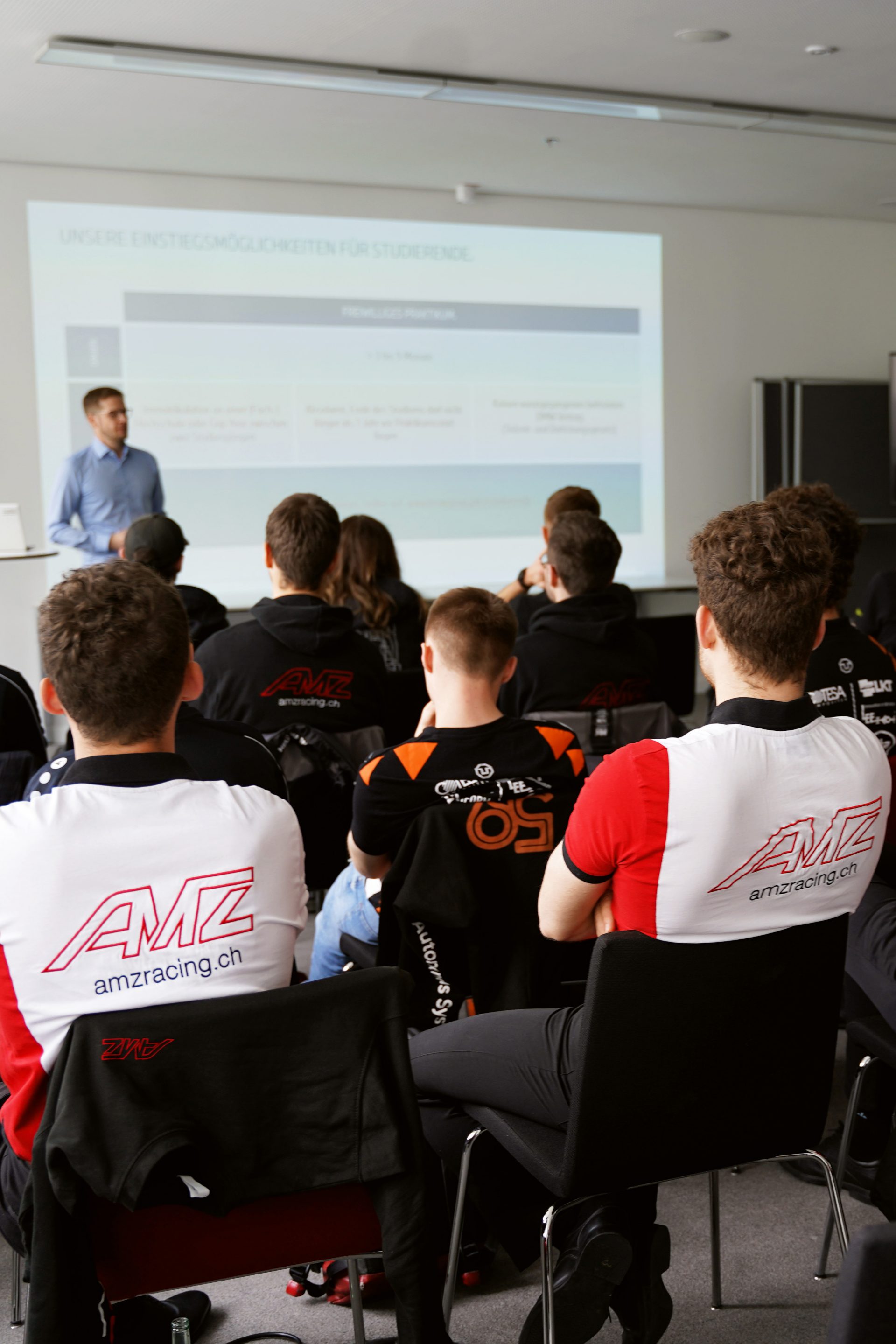 Das AMZ racing team sitzt zusammen und schaut sich eine Präsentation an.