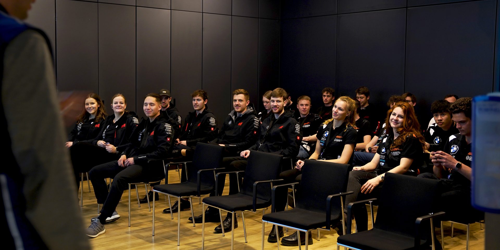 Das Rennteam sitzt in einem dunklen Raum, um sich eine Präsentation anzuschauen.