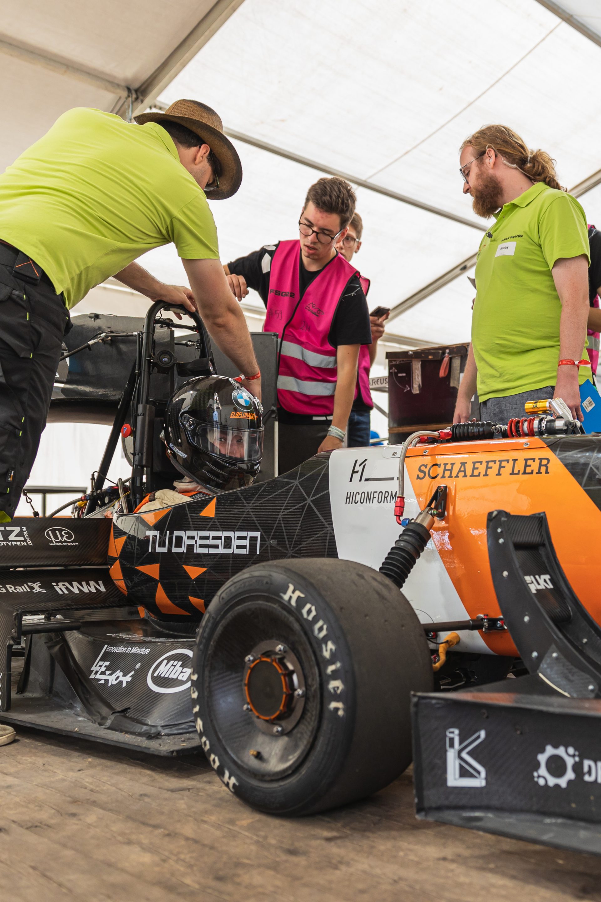 Der Rennfahrer sitzt im Rennwagen während sein Team den Wagen inspiziert.