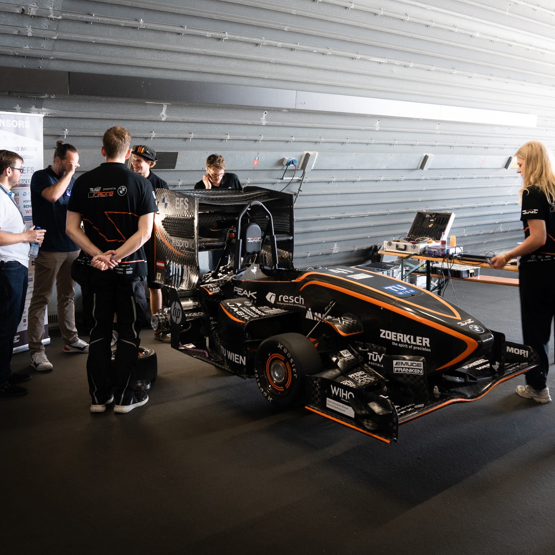 EIne Gruppe junger Leute steht um ein Rennauto herum.