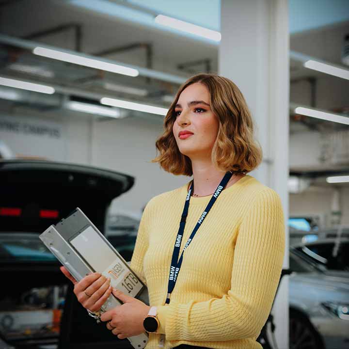 Eine Praktikantin geht mit einem Ordner in der Hand durch eine BMW Group Werkstatt.
