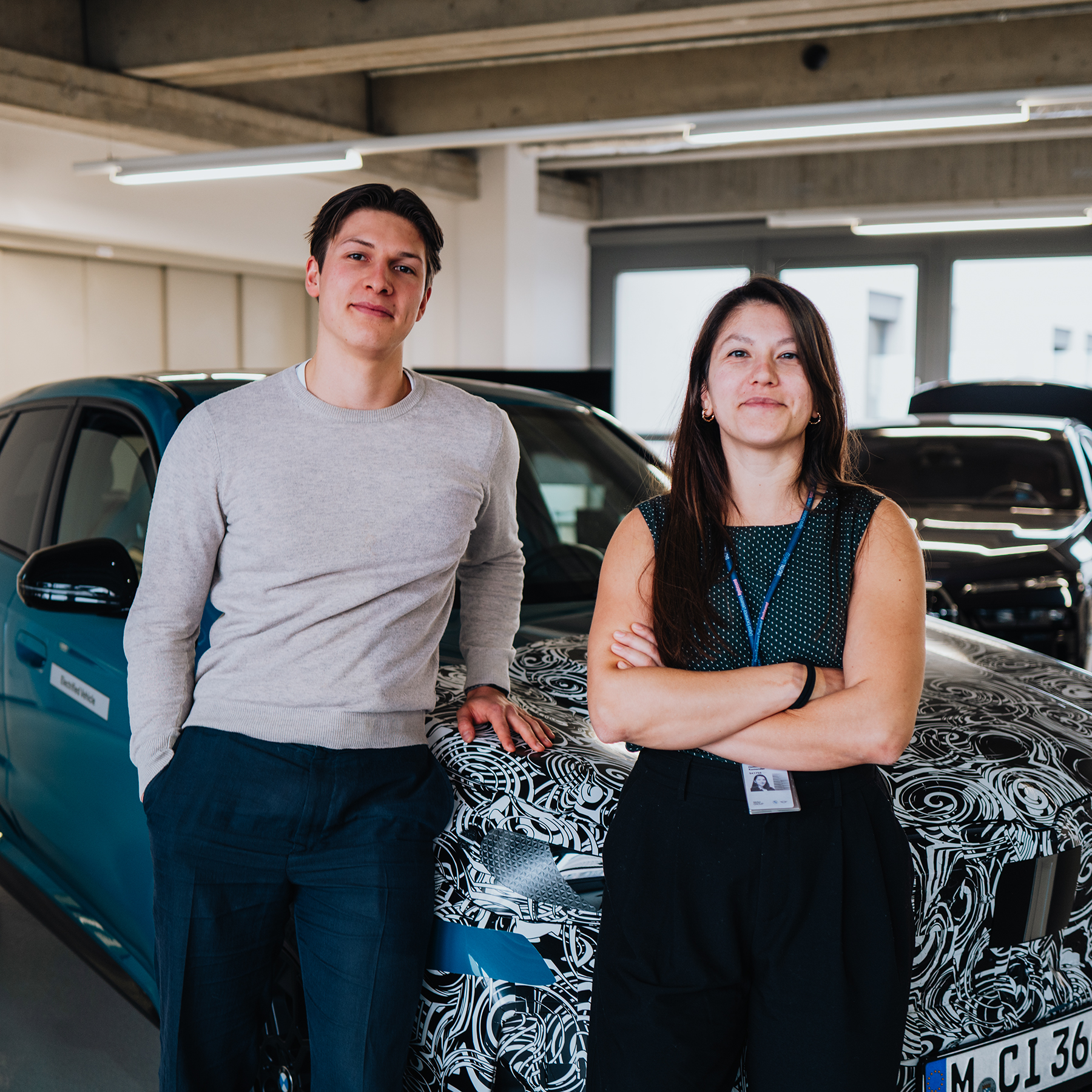 Arne und Dominique lehnen an ein getarntes Fahrzeug in einer Entwicklungsumgebung.