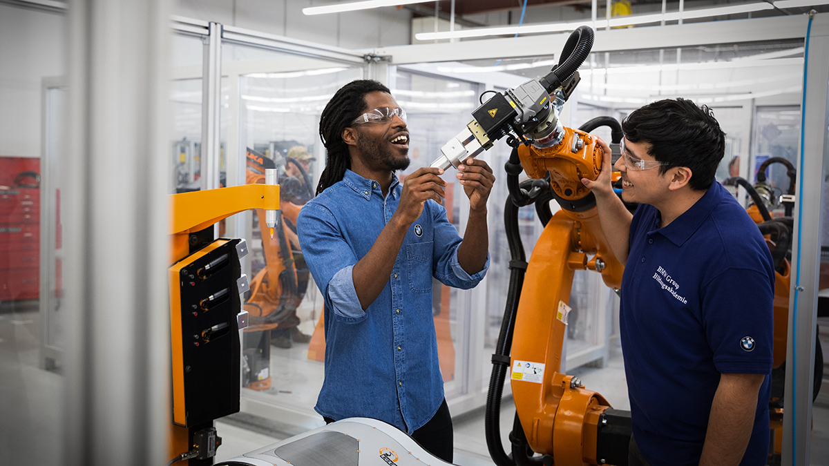 Zwei Auszubildende der BMW Group arbeiten an einem Roboterarm.