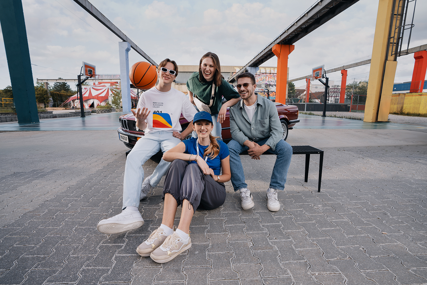 Urbaner Spielplatz mit Freunden und einem alten BMW Auto im Hintergrund.
