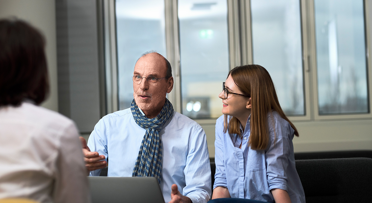 Das Foto zeigt ein Gespräch zwischen einem Senior Experten bei BMW und zwei jüngeren Mitarbeiterinnen.