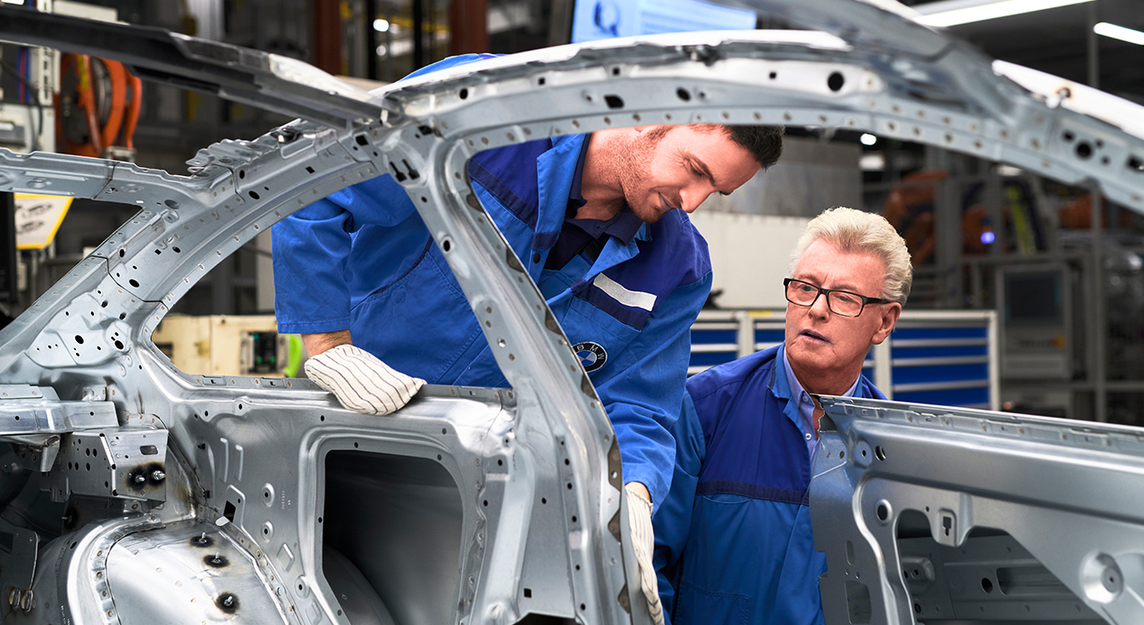 Das Foto zeigt zwei Mitarbeiter bei der Qualitätskontrolle einer Karosserie eines BMWs.