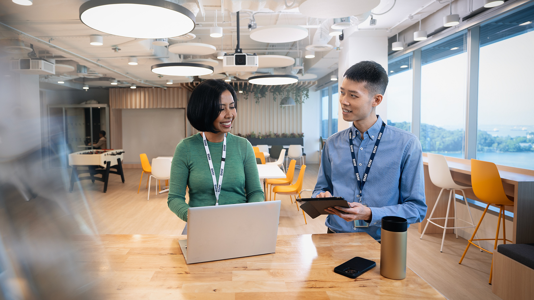 Zwei Mitarbeiter:innen der BMW Group unterhalten sich in einer modernen und hellen Büroumgebung mit großen Fenstern.
