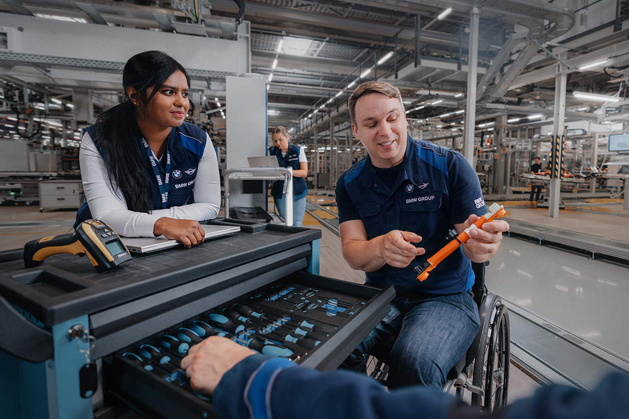 Drei Kolleg:innen, einer davon im Rollstuhl, in der Produktionshalle bei der BMW Group