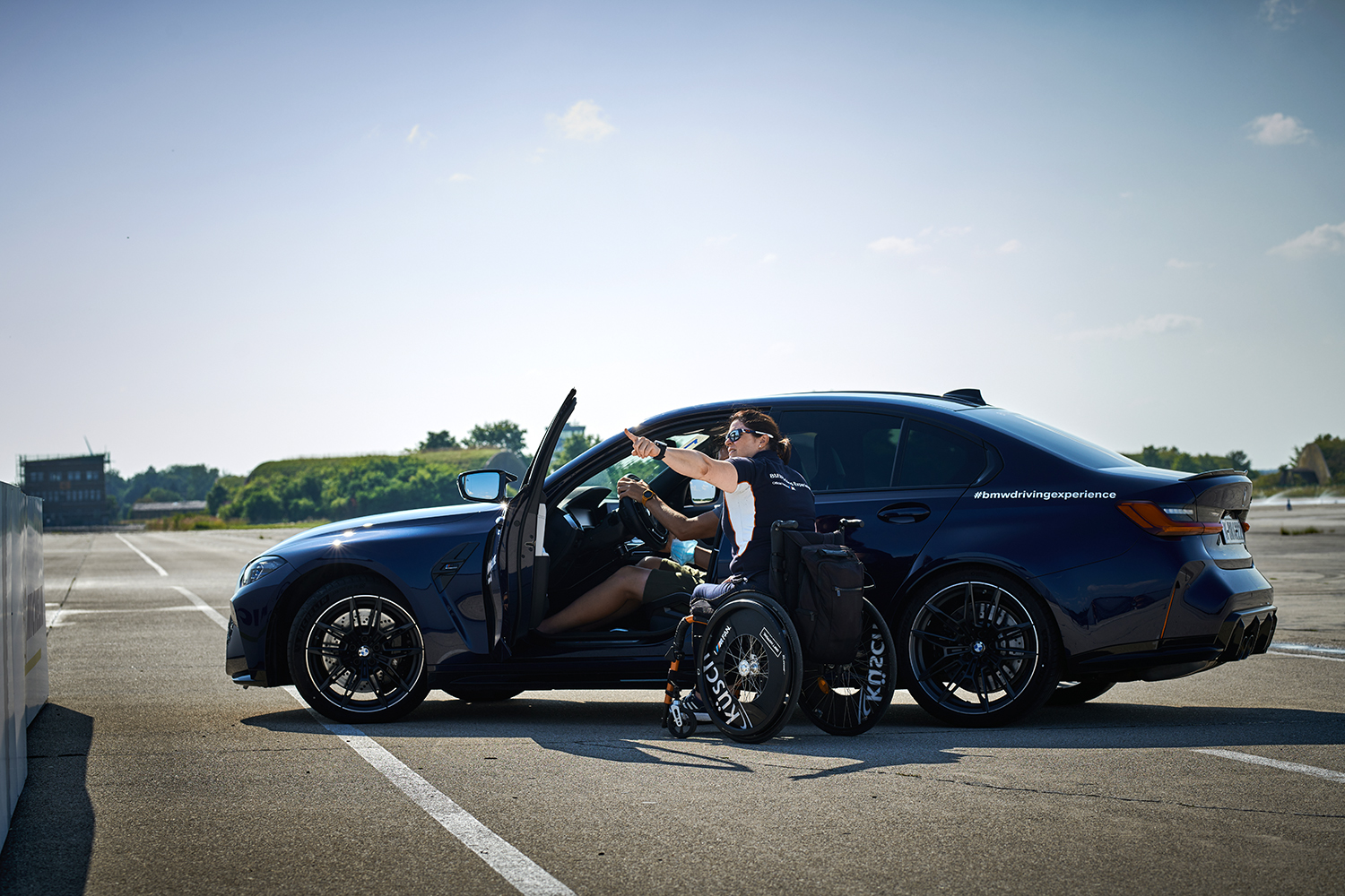 BMW Mitarbeiterin Tina im Rollstuhl vor einem Auto der BMW Driving Experience