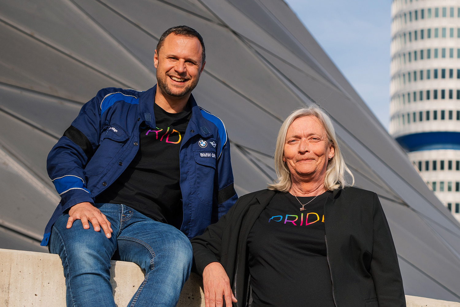 Zwei Vertreter:innen des BMW Group Pride Netzwerks vor dem BMW Vierzylinder in München