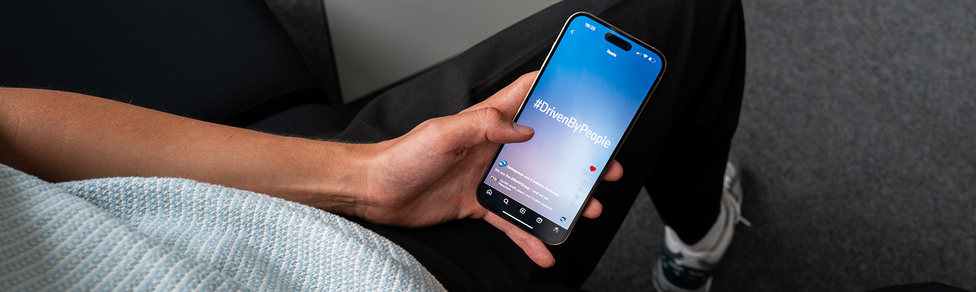 Ein Mann schaut auf sein Handy, auf dem ein Post mit #DrivenByPeople zu sehen ist