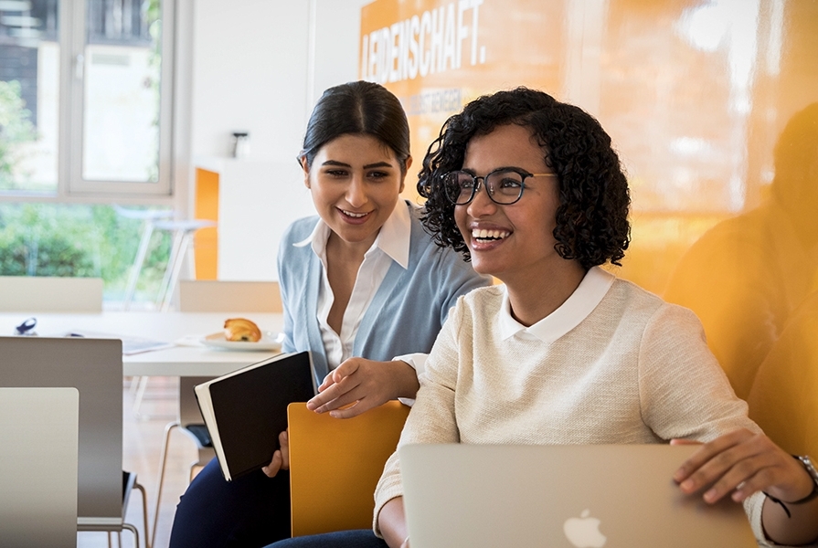 Zwei junge Frauen bei der BMW Group lachen zusammen bei der Arbeit.