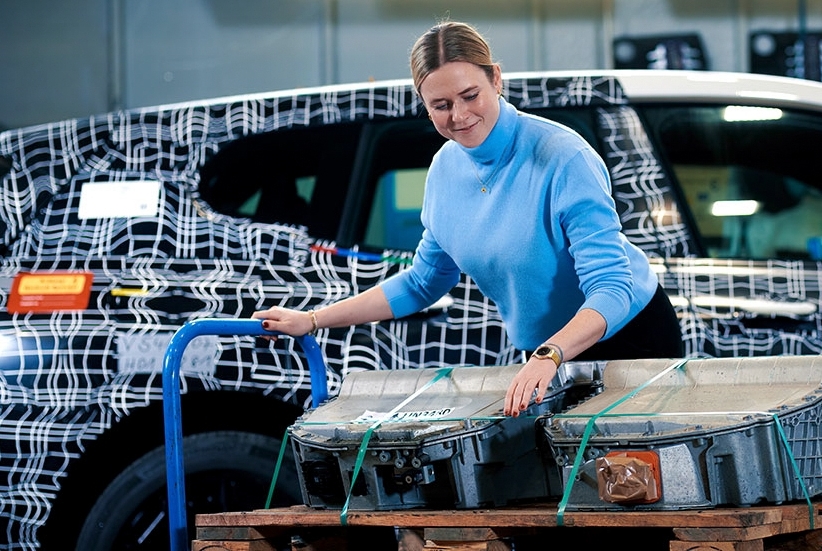 Eine BMW Mitarbeiterin bei der Arbeit an Fahrzeugteilen neben einem Elektrofahrzeug.