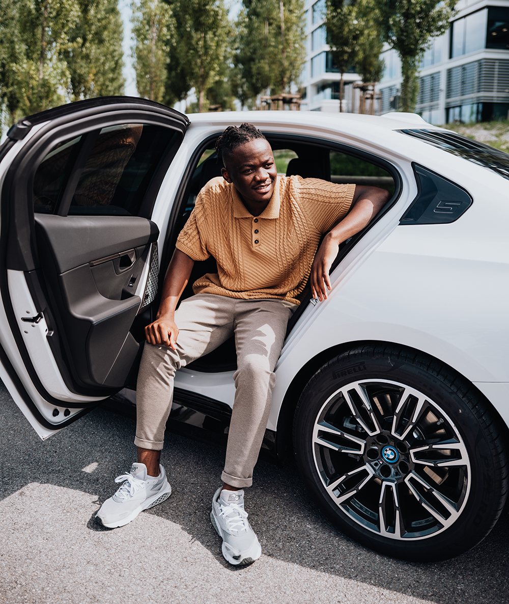 Der Werkstudent lehnt von außen an der Rückbank eines BMW i5 und schaut zur Seite