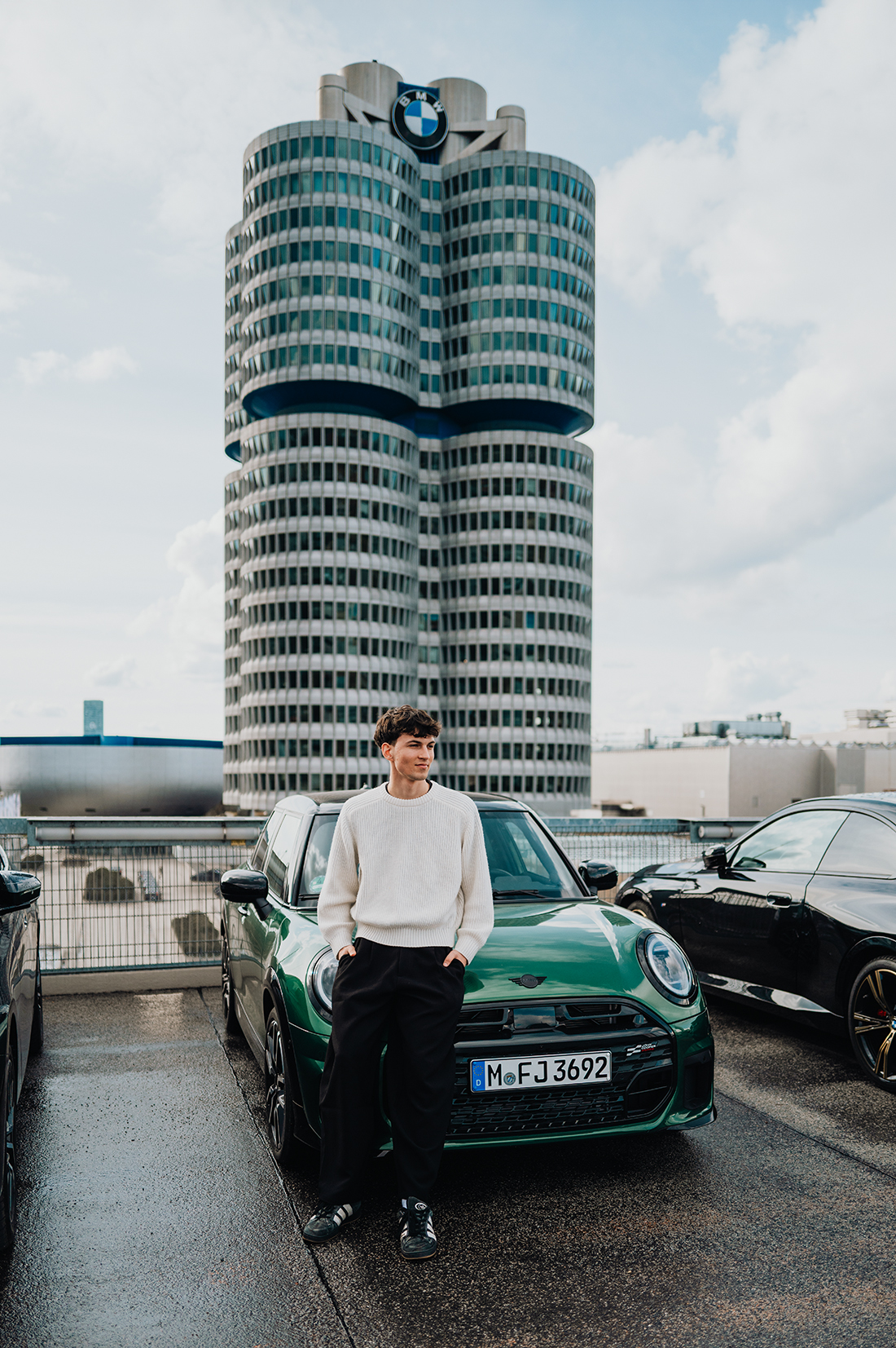 Dualer Student Anton lehnt an einem grünen MINI vor dem BMW Vierzylinder