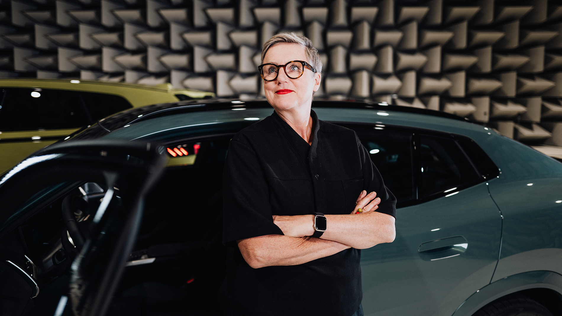 Daniela mit verschränkten Armen vor dem BMW iX2 und schaut zufrieden in die Ferne.