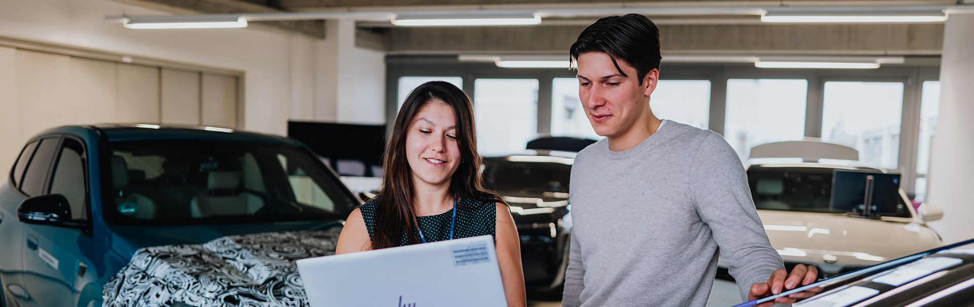 Arne und Dominique diskutieren Inhalte auf einem Laptop vor verschiedenen Prototyp Fahrzeugen.