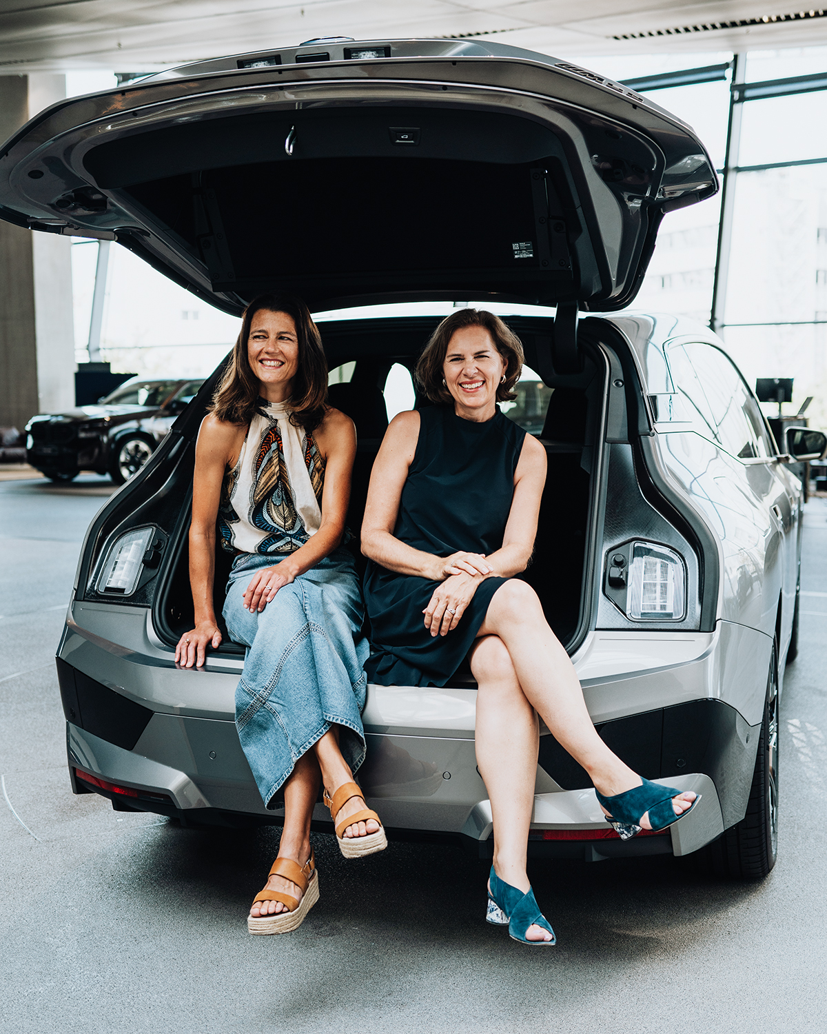 Die Zwei Frauen im Führungs-duo sitzen zusammen im Kofferaum eines BMW iX.