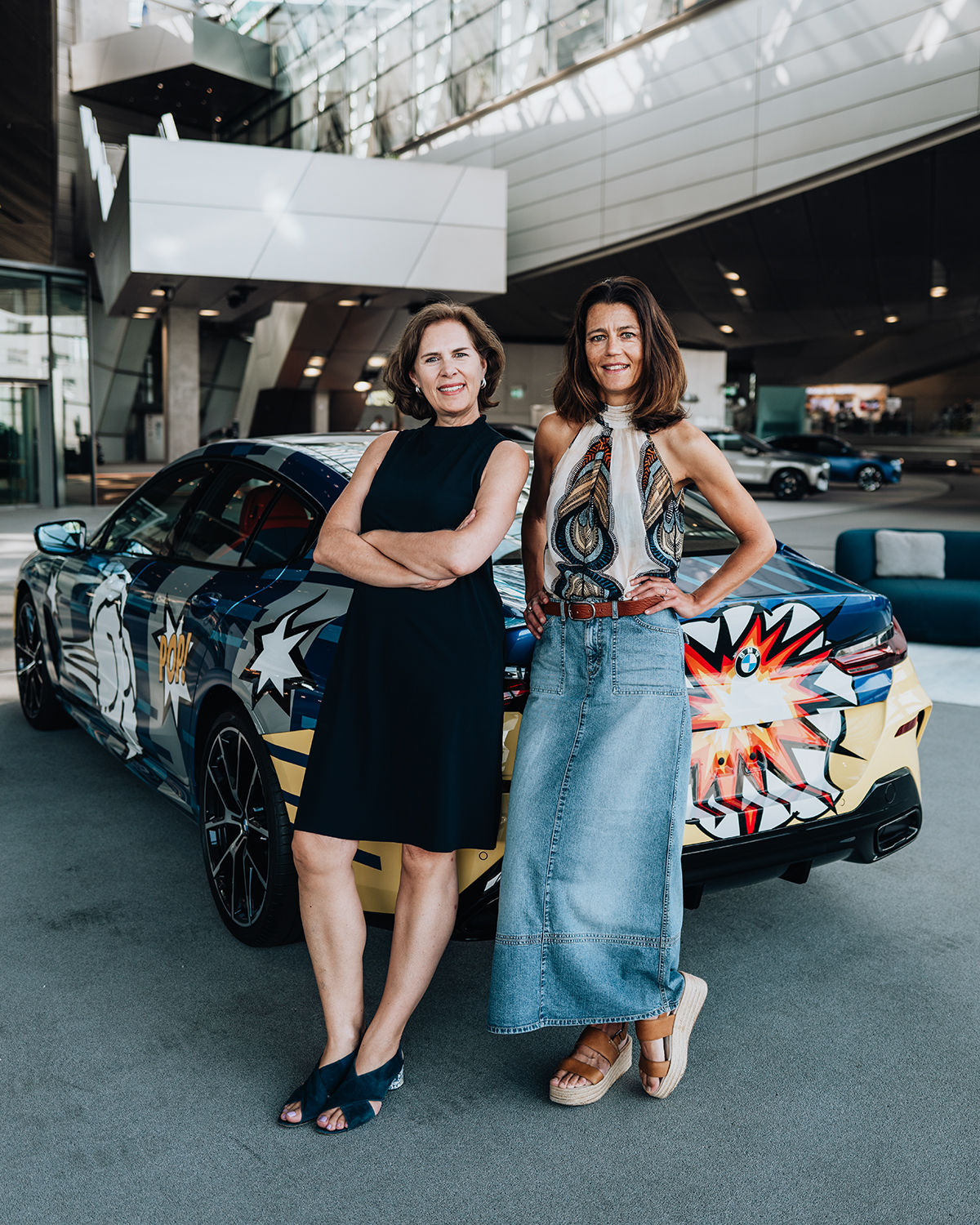 Die zwei Frauen posieren zusammen vor einem bemalten BMW M8.