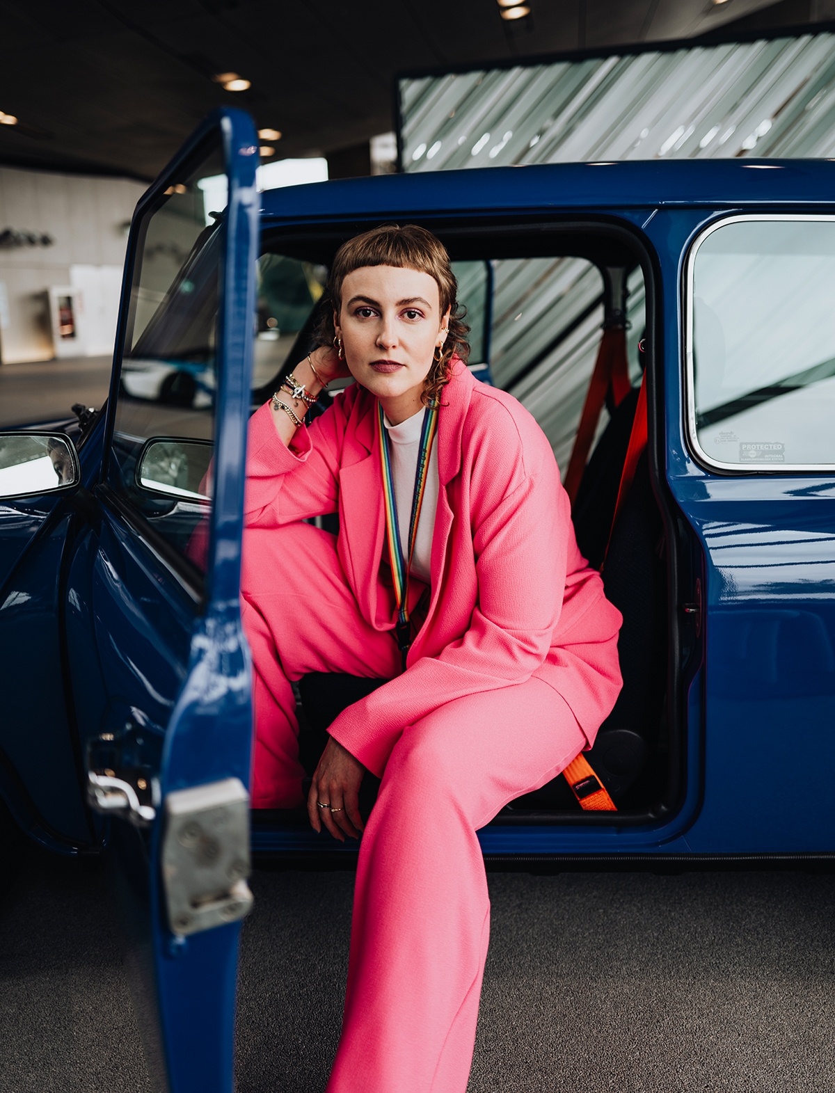 Praktikantin in pinkem Anzug im dunkelblauen Oldtimer-MINI.