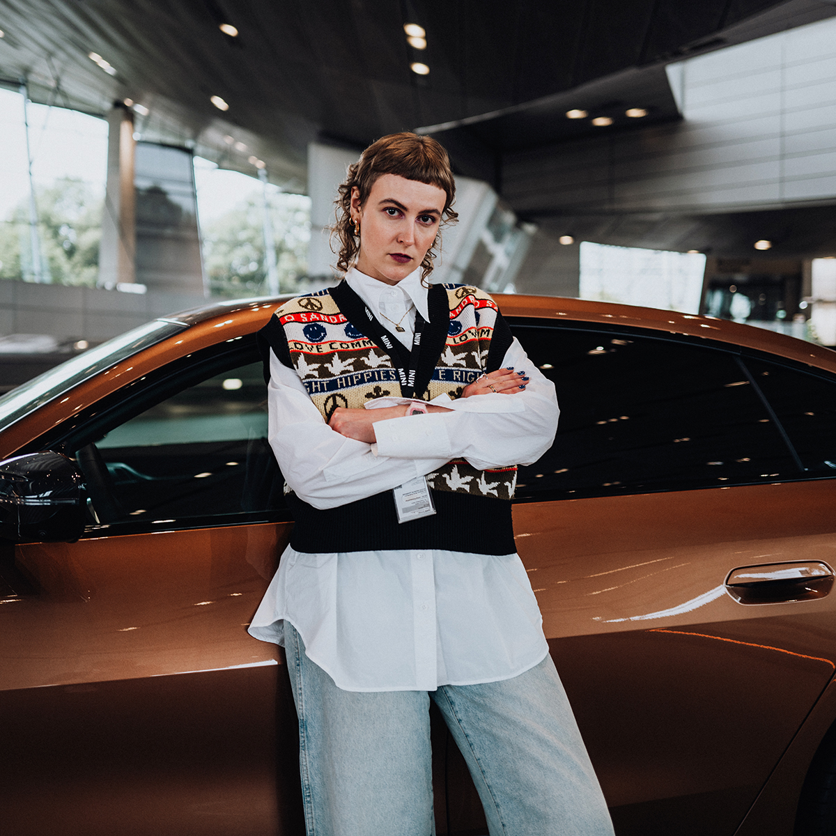 Die Praktikantin steht neben einem braunen BMW M3 in der BMW Welt.