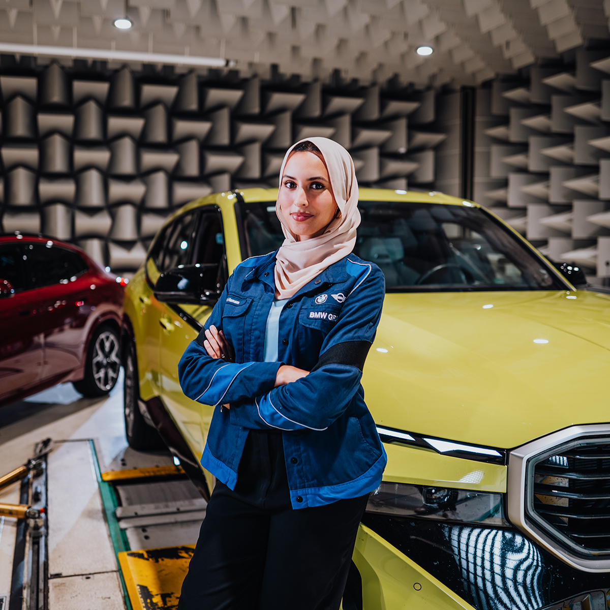 Ines posiert mit verschränkten Armen vor einem gelben BMW XM.