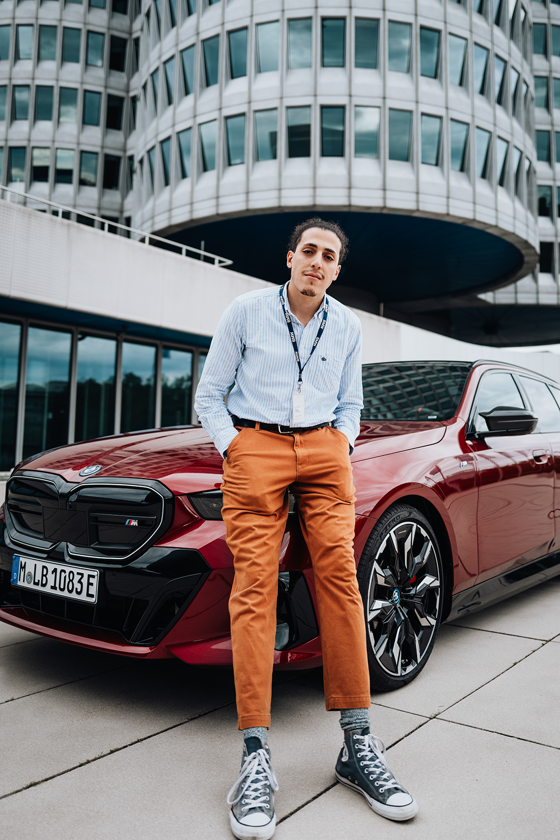 Der BMW Group Mitarbeiter steht mit einem BMW i5 vor dem Vierzylinder in München