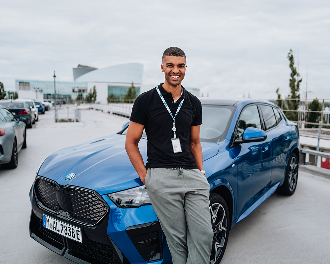 Ingenieur der BMW Group lehnt an einem blauen BMW iX2.