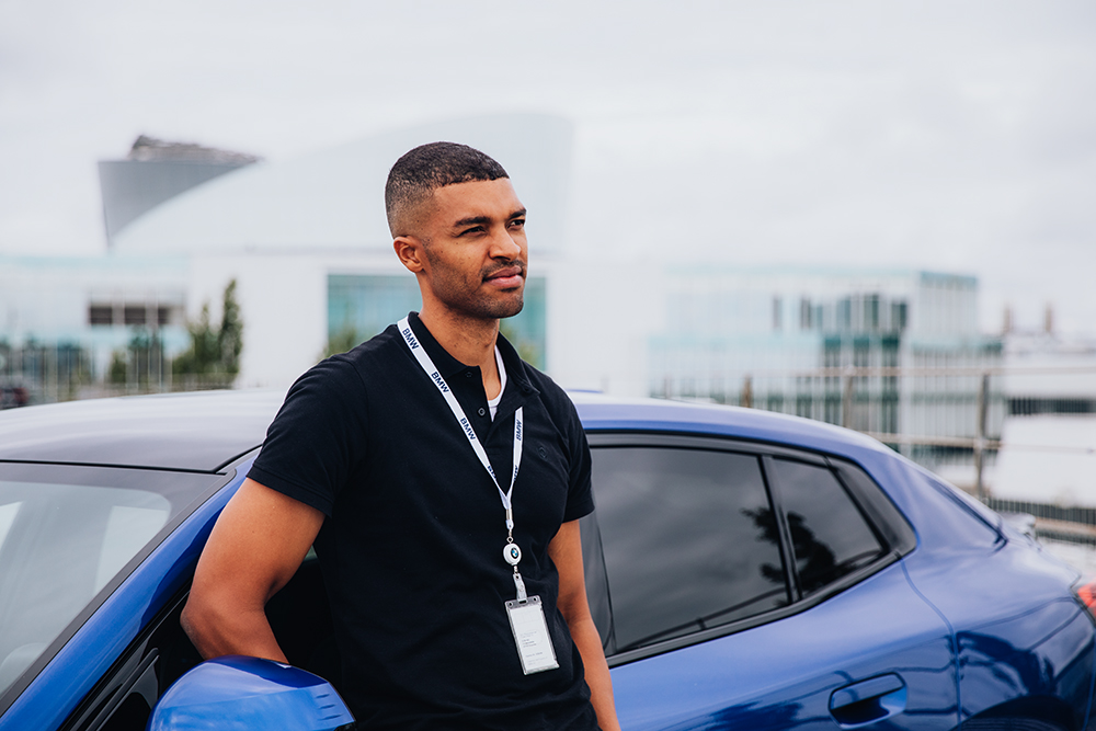 Ingenieur der BMW Group lehnt an der Fahrertür eines blauen BMW iX2.
