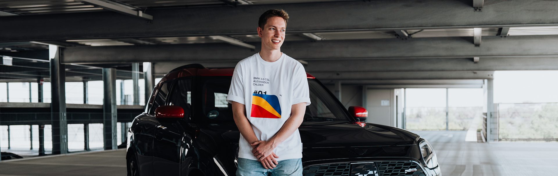 Ein Masterand bei der BMW Group lehnt an der Motorhaube eines schwarz-roten MINI Countryman.