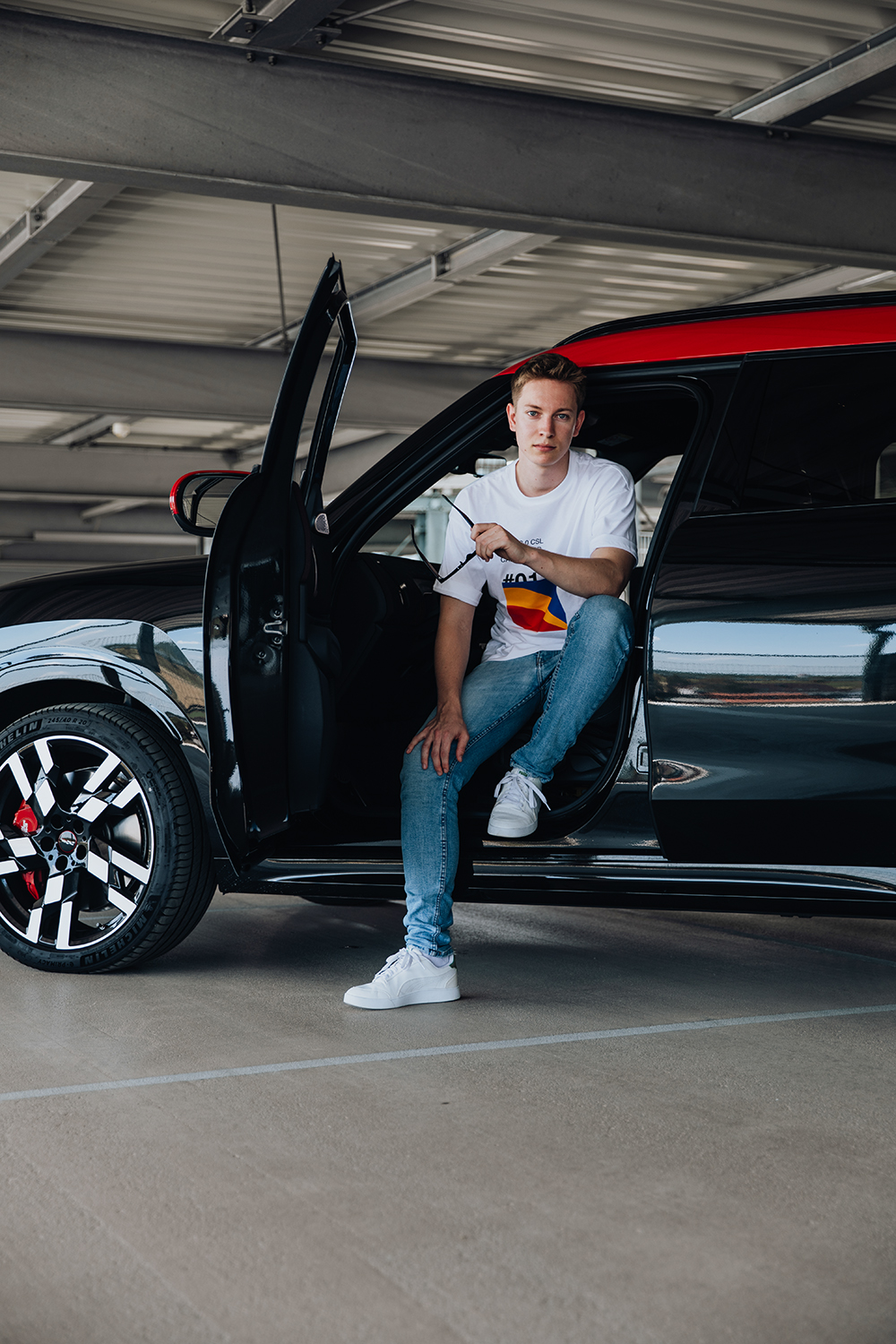 Der Masterand sitzt auf dem Fahrersitz eines schwarz-roten MINI Countryman mit einem Fuß draußen auf dem Boden.