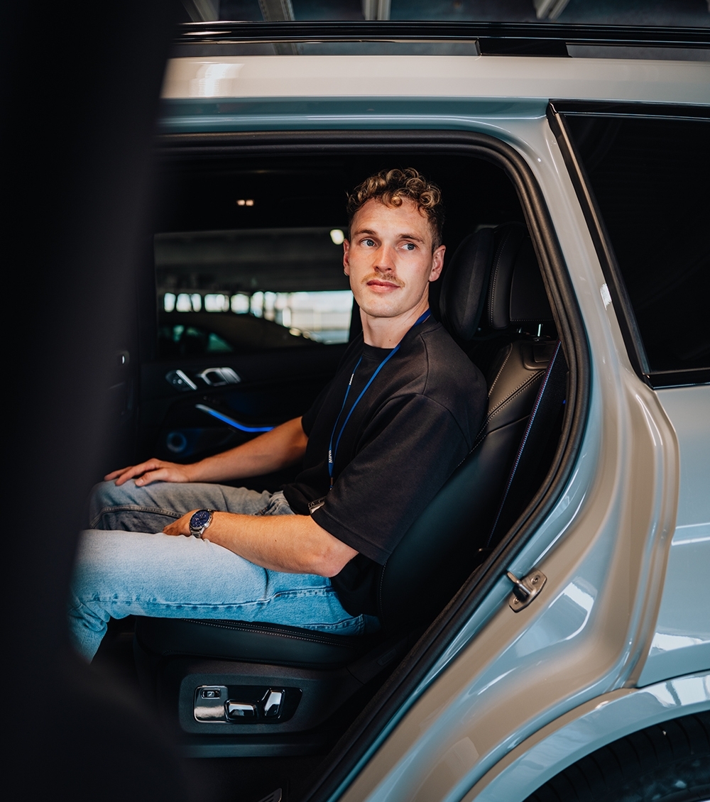 Ingenieur der BMW Group sitzt auf dem Rücksitz und schaut in die Kamera.
