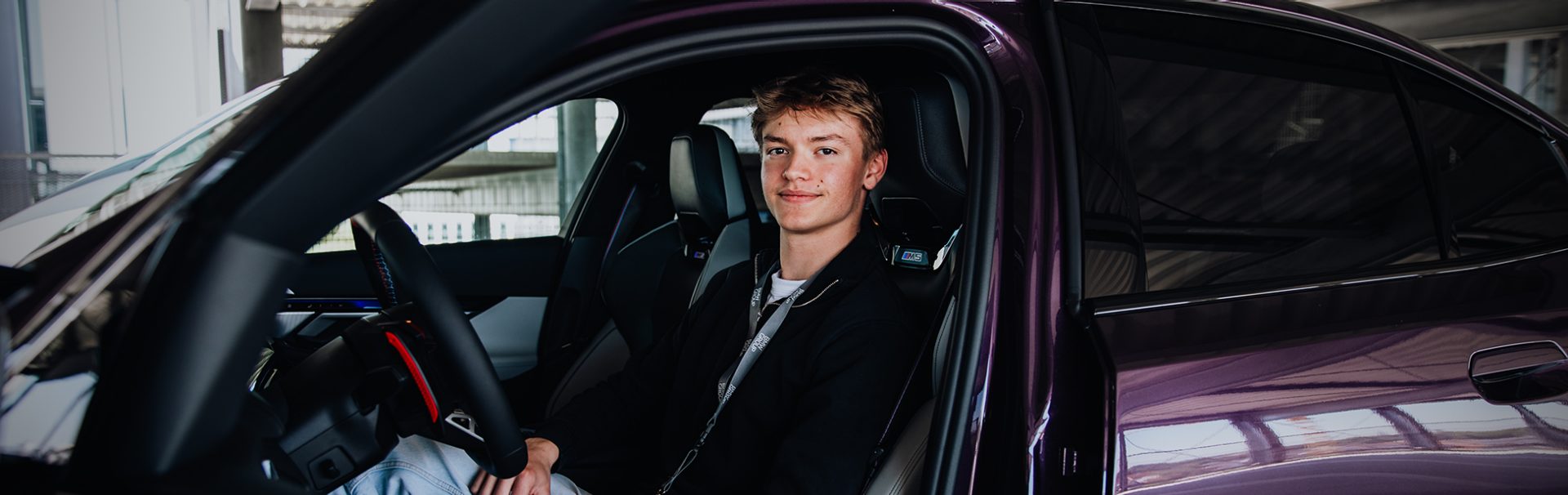 Azubi Tobias auf dem Fahrersitz eines BMW M5 in Lila