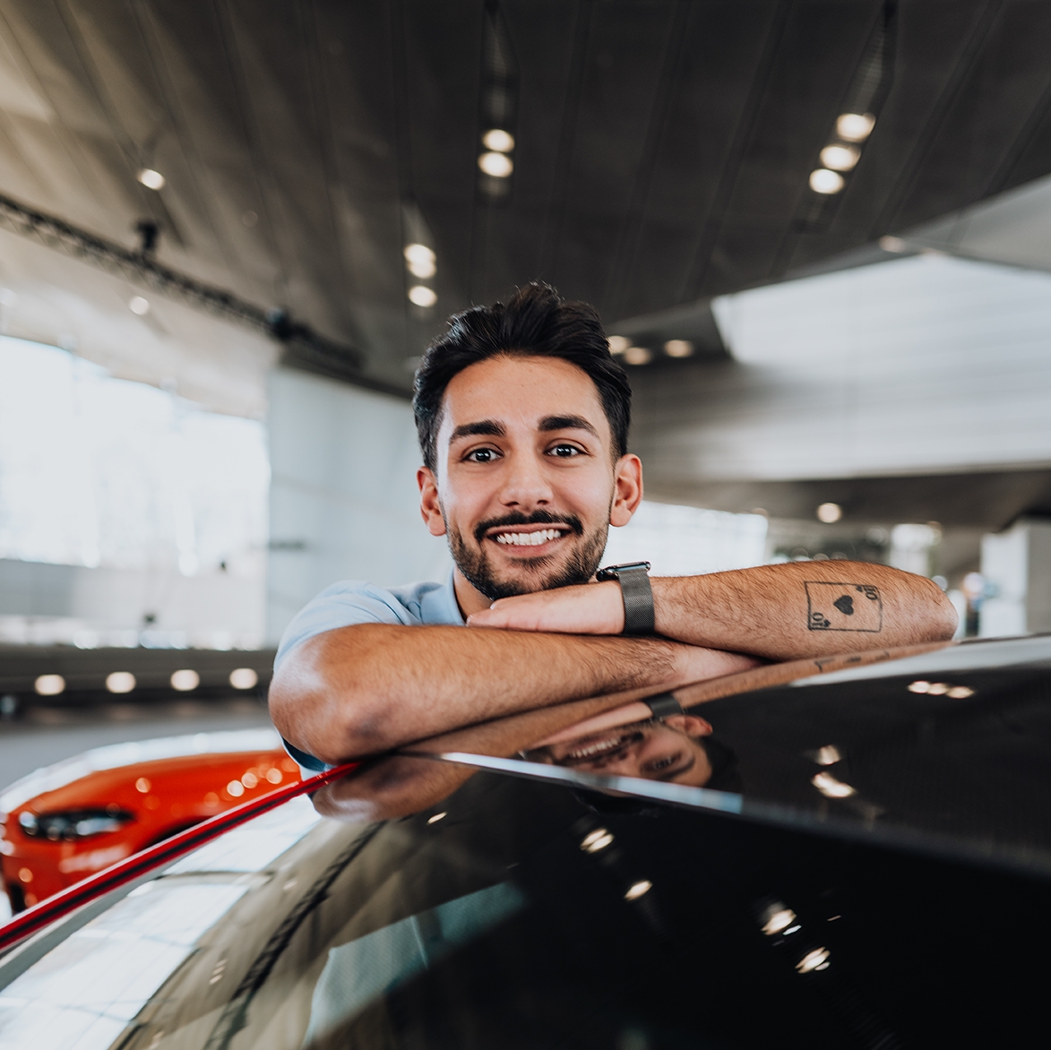 BMW Mitarbeiter Yasar lehnt an einem BMW M5 und lacht über das Dach hinweg