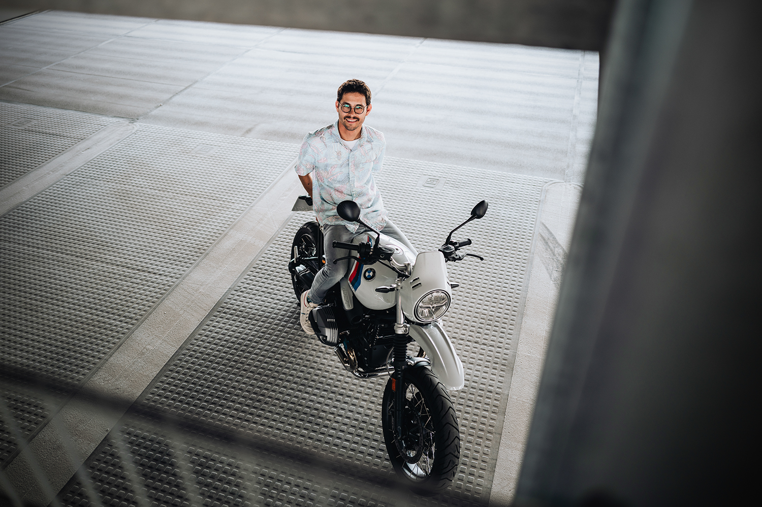 Mitarbeiter sitzt auf einem BMW Motorrad und lächelt nach oben in die Kamera.